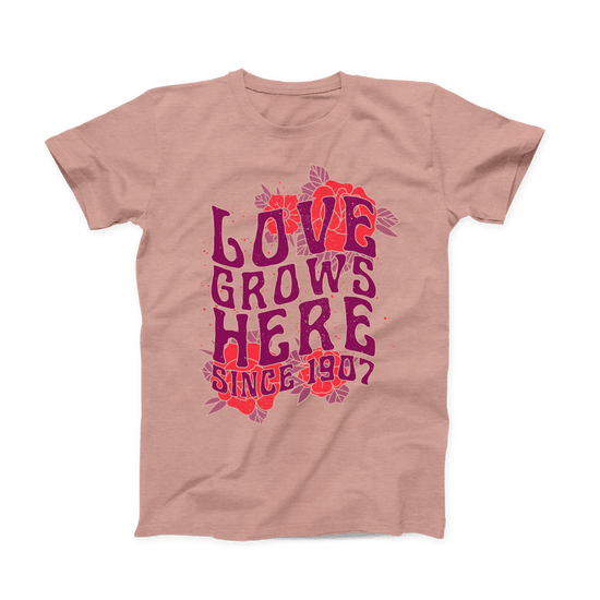 Heather Prism Peach colored Oklahoma T-shirt. Large design across the whole front of the shirt with red roses in the background of the top and bottom. "LOVE GROWS HERE" in a stacked purple font with "Since 1907" below it.