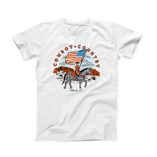 White OSU T-shirt with orange, grey, blue and black design printed on the front. The circular design is a cowboy on horseback holding the American flag. "Cowboy (star) Country" is written above the design in a half circle, in orange bold font. And "Stillwater, OK" is written in small black script font at the bottom. 