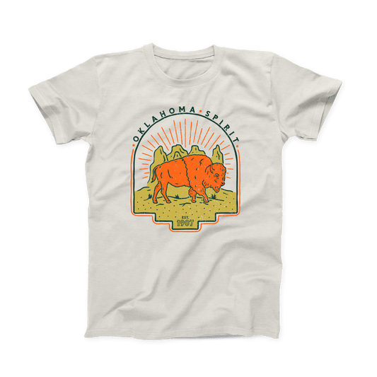 Natural colored Oklahoma T-shirt. Screen printed in gold, orange and navy. An orange bison is depicted in front of a gold canyon with the sun's rays shining behind it. In thin, curved font above the scene is "OKLAHOMA SPIRIT" in navy. And below the scene is "Est. 1907" in small font.