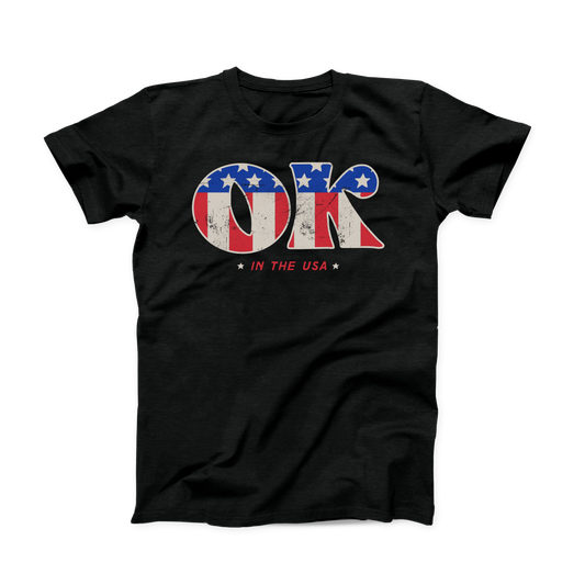 Solid black colored Oklahoma t-shirt. Screen printed in a vintage, distressed style is a large "OK" with the American flag print inside the letters.  And in smaller font below is "IN THE USA" in red with a small white star on either side. 