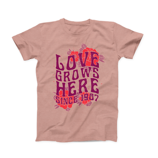 Heather Prism Peach colored Oklahoma T-shirt. Large design across the whole front of the shirt with red roses in the background of the top and bottom.  "LOVE GROWS HERE" in a stacked purple font with "Since 1907" below it. 