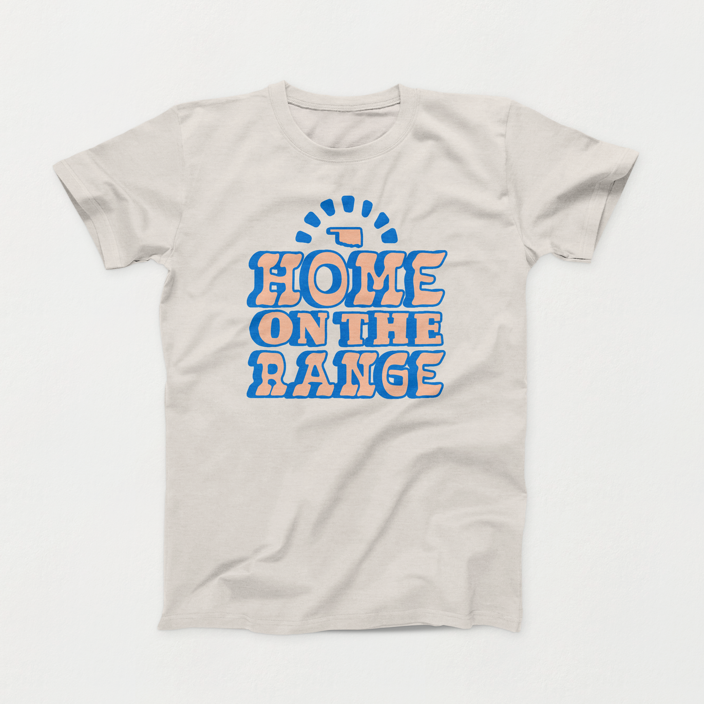 Light Heather Cement colored Oklahoma T-shirt. In stacked font printed in blue and light orange is "HOME," "ON THE," "RANGE." Above the words is a small state symbol.