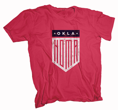 Red colored Oklahoma t-shirt. Screen printed in a vintage, distressed style shield in white and navy. The top of the shield is a rectangle of Navy with "OKLA" between 2 stars in white font. The bottom portion of the shield is printed in white with "HOMA" stretched out to fill the whole space, top to bottom, in red. 