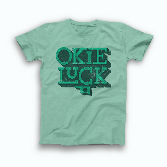Mint green colored Oklahoma T-shirt. Screen printed in a distressed, vintage style in green with a dark green background is "OKIE" stacked atop "LUCK" with a small OK state symbol below and a 4 leaf clover inside the state. 